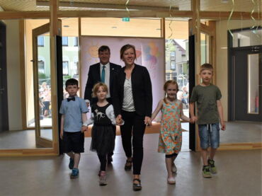 Das Foto zeigt wie vier Kinder sich an den Händen haltend - in ihrer Mitte die Kitaleiterin Kathleen Michel - in die Kita gehen. Ihnen folgt im Hintergrund Oberbürgermeister Sven Mißbach.