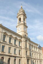 Das Foto zeigt eine Außenaufnahme des heutigen dreigeschossigen Rathauses von Großenhain. Man sieht viele Fenster und den Rathausturm.