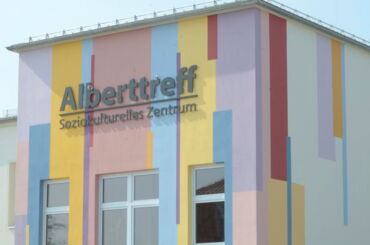Das Foto zeigt ein farbiges Gebäude. An der Außenfassade steht: Alberttreff. Soziokulturelles Zentrum