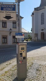Das Foto zeigt den Parkscheinautomaten auf der Naundorfer Straße. Im Hintergrund erkennt man den Kirchplatz und die Marienkirche.
