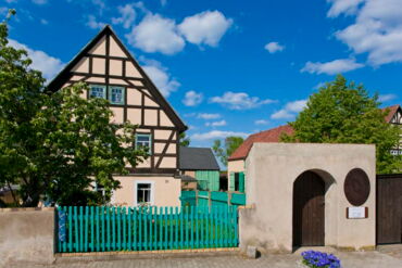 Das Foto zeigt eine Außenaufnahme des Bauernmuseums in Zabeltitz. Auf der linken Seite sieht man das Haupthaus, rechts daneben das Eingangstor.