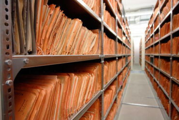 Das Foto zeigt einen der Magazinräume des Stasi-Unterlagen Archivs in Berlin. Man sieht lange Regale, die mit Akten gefüllt sind.