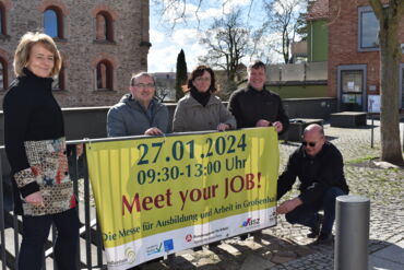 Das Foto zeigt fünf Personen. Sie blicken in die Kamera und halten dabei ein Banner auf dem Daten und Uhrzeit der Jobmesse "Meet your JOB" stehen.