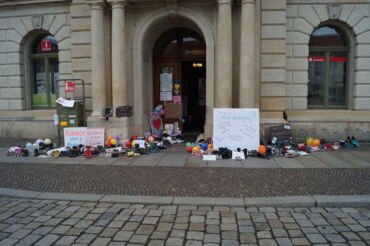 Das Foto zeigt den Haupteingang des Großenhainer Rathauses. Auf der linken und rechten Seite stehen dutzende Schuher und sind eine Reihe von Plakaten zu sehen.